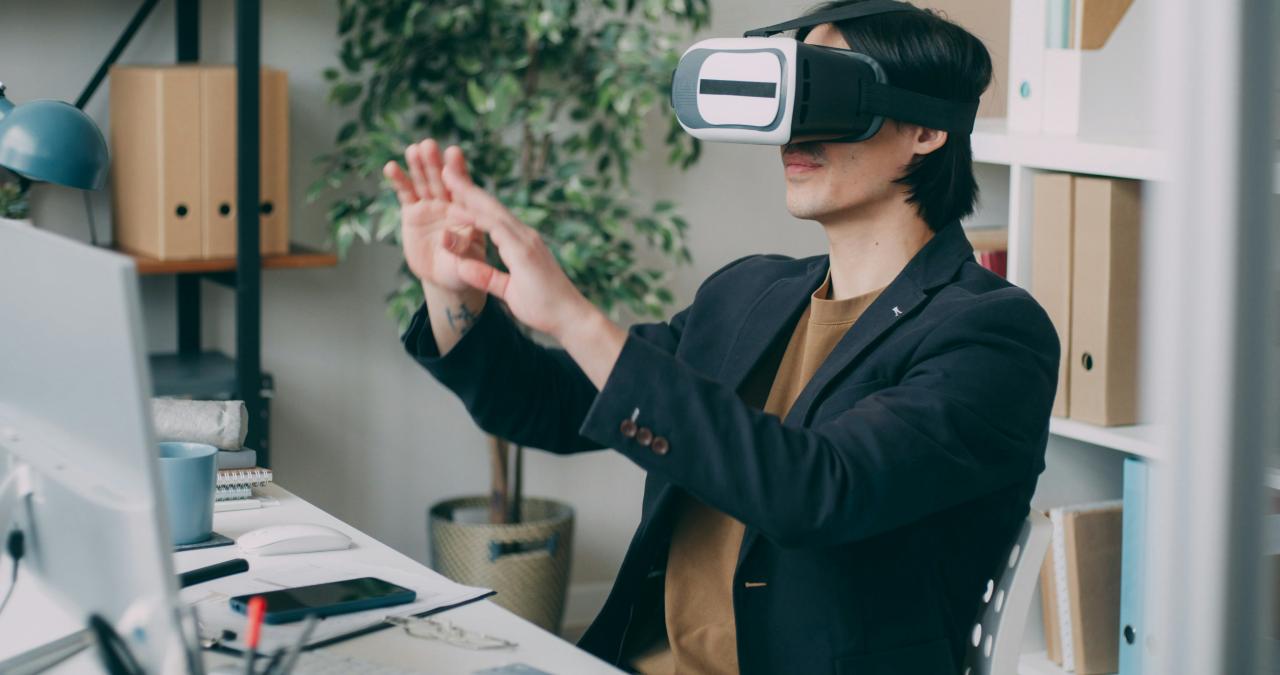 A woman wearing a virtual headset standing in front of a computer